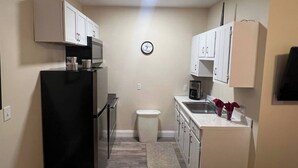 A compact kitchen with white cabinets, a black refrigerator, a microwave, and a sink. - cozy elegant efficiency (Harrisburg)