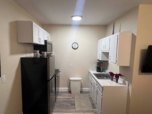 Una cocina compacta con armarios blancos, un refrigerador negro, un microondas y un lavabo.