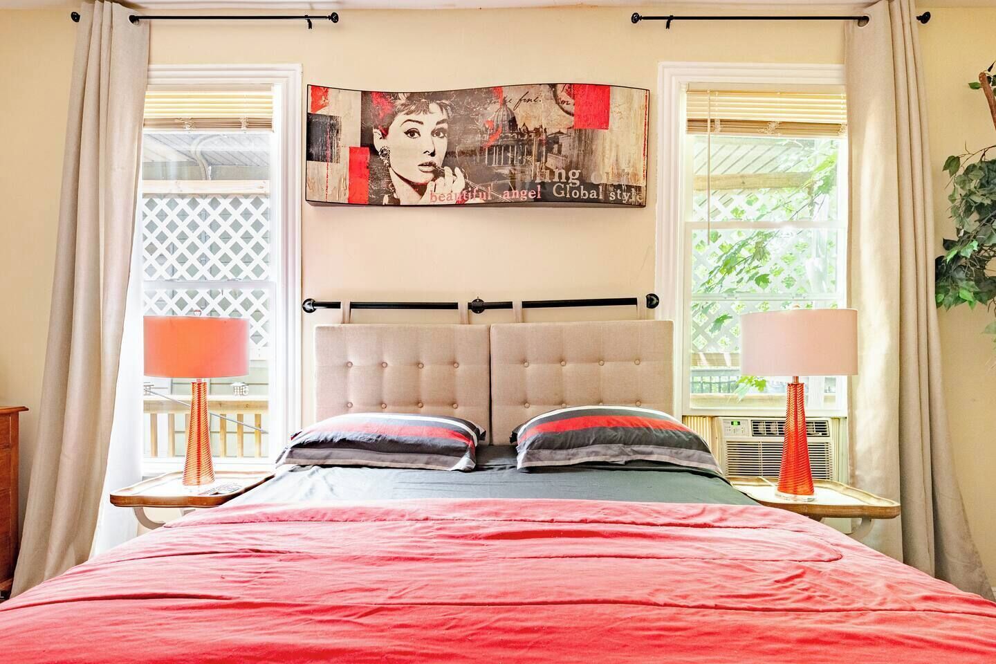 Un dormitorio con una cama, dos lámparas de noche, una ventana con cortinas y una obra de arte colgada en la pared.