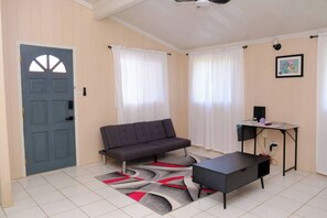 Ein Zimmer mit grauem Sofa, einem kleinen Tisch, einem Schreibtisch und einer Tür mit markantem Design.