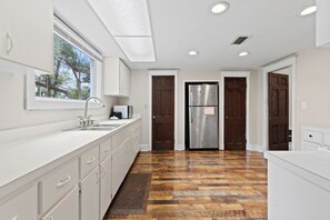 A modern kitchen with white cabinetry, stainless steel appliances, and a herringbone wood floor. - Historic 1935 Charmin Retreat 4BR Near Devil’s Den and Cedar Lake (Williston)