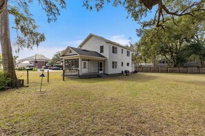 A two-story house with a covered porch, a fenced yard, and a wooden fence in the background. - Historic 1935 Charmin Retreat 4BR Near Devil’s Den and Cedar Lake (Williston)