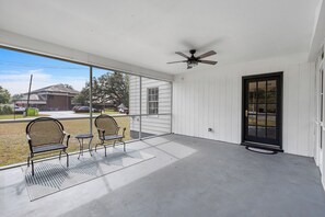 A covered porch with two chairs and a table, a ceiling fan, and a view of the street. - Historic 1935 Charmin Retreat 4BR Near Devil’s Den and Cedar Lake (Williston)