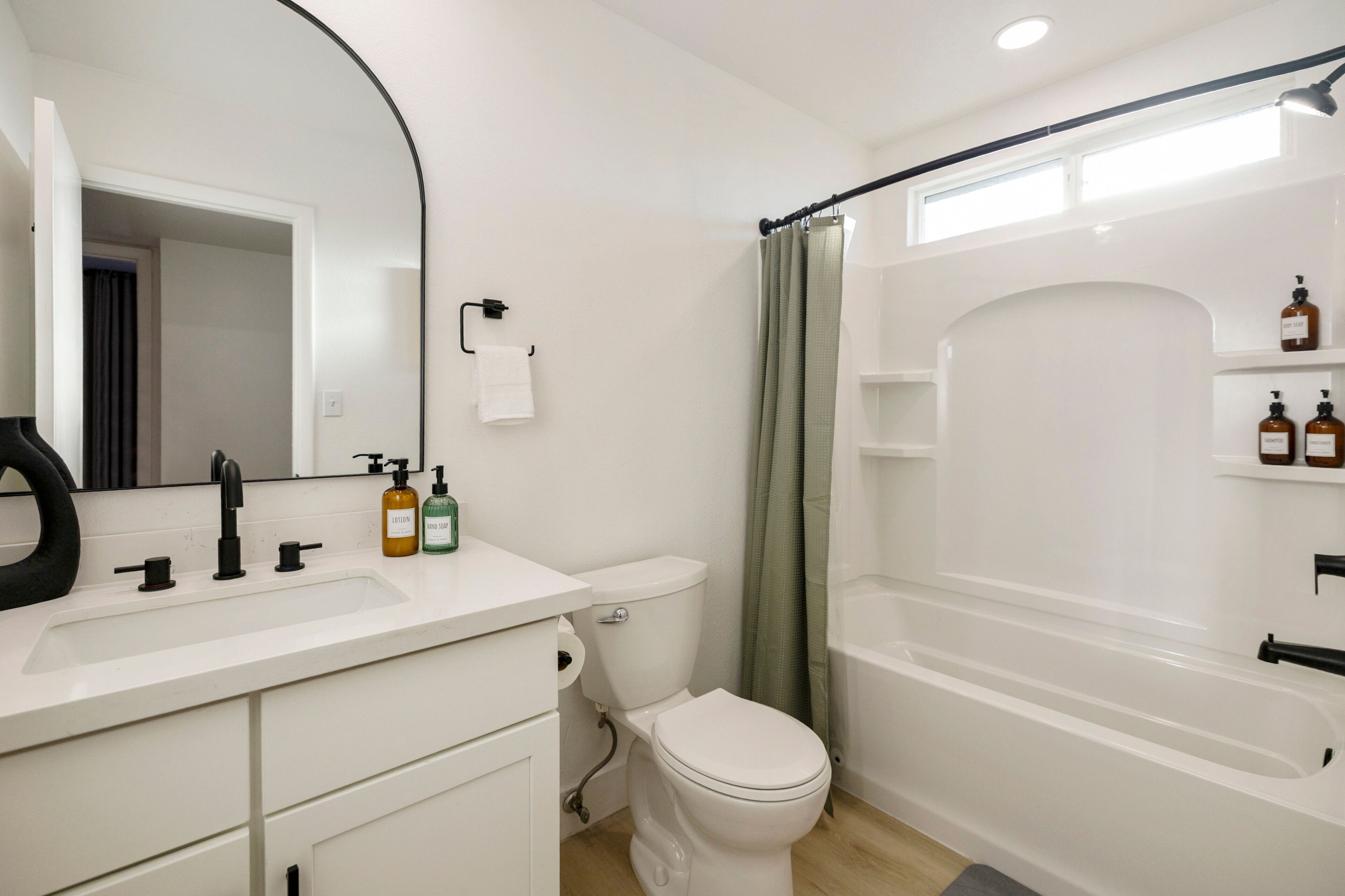 Un baño moderno con lavamanos, inodoro y bañera blancos. Hay artículos de aseo en la encimera y una cortina de ducha.