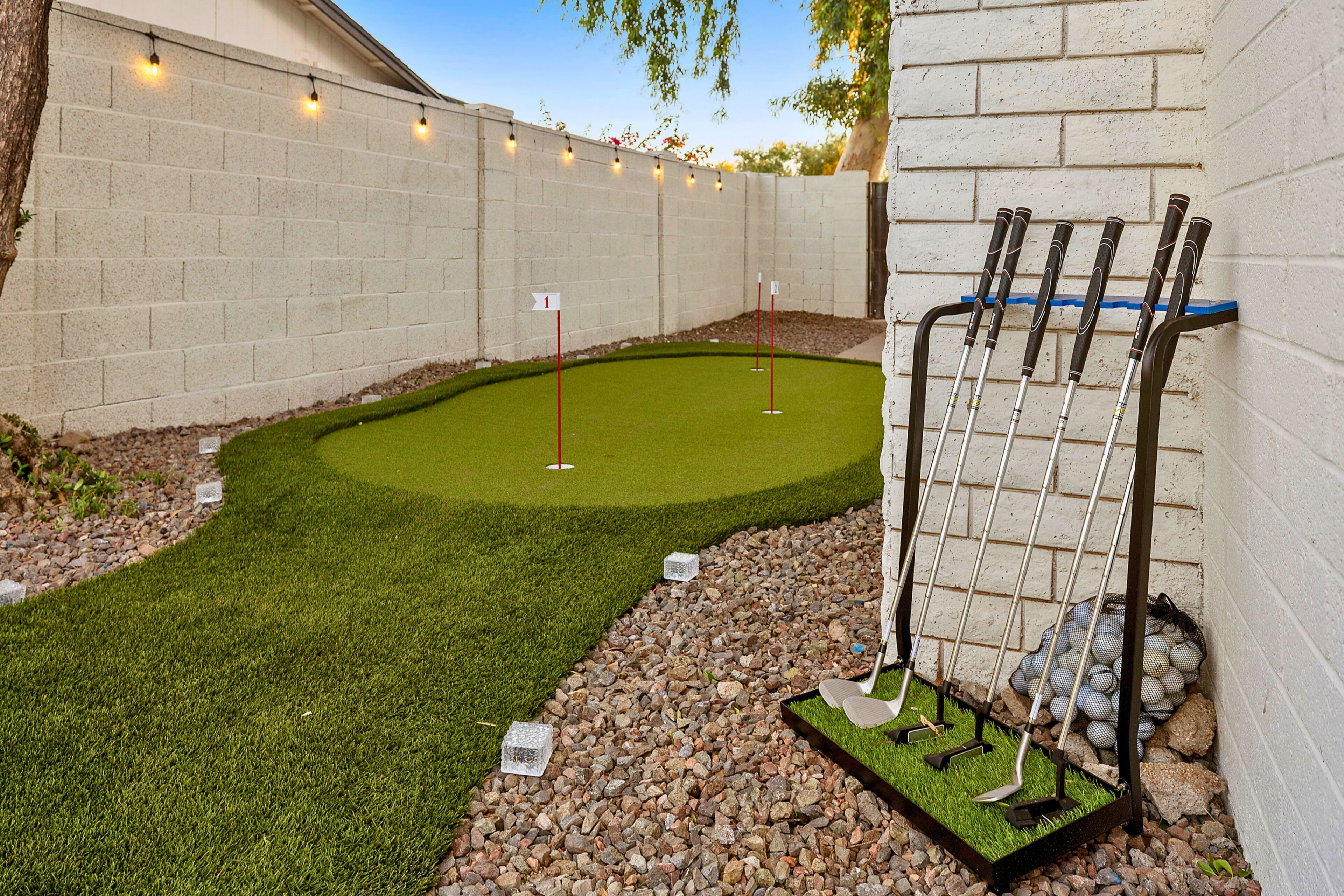 Un campo de mini golf con un putting green, una zona de arena y un portaequipajes metálico para palos de golf.