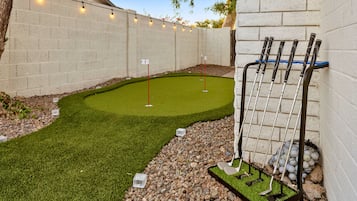 Un campo de mini golf con un putting green, una zona de arena y un portaequipajes metálico para palos de golf.