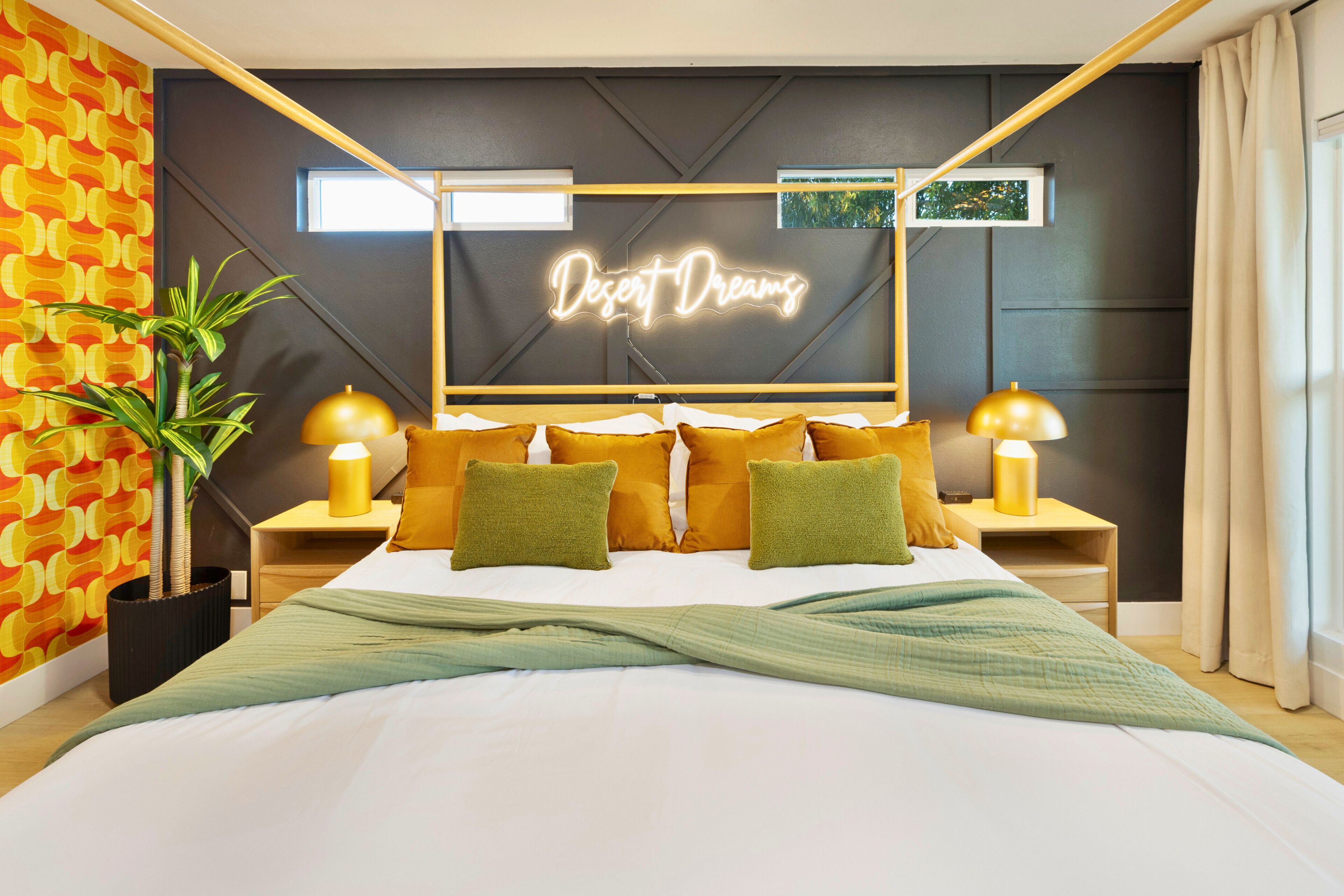 A modern bedroom with a bed, two bedside tables, a neon sign, and a potted plant.