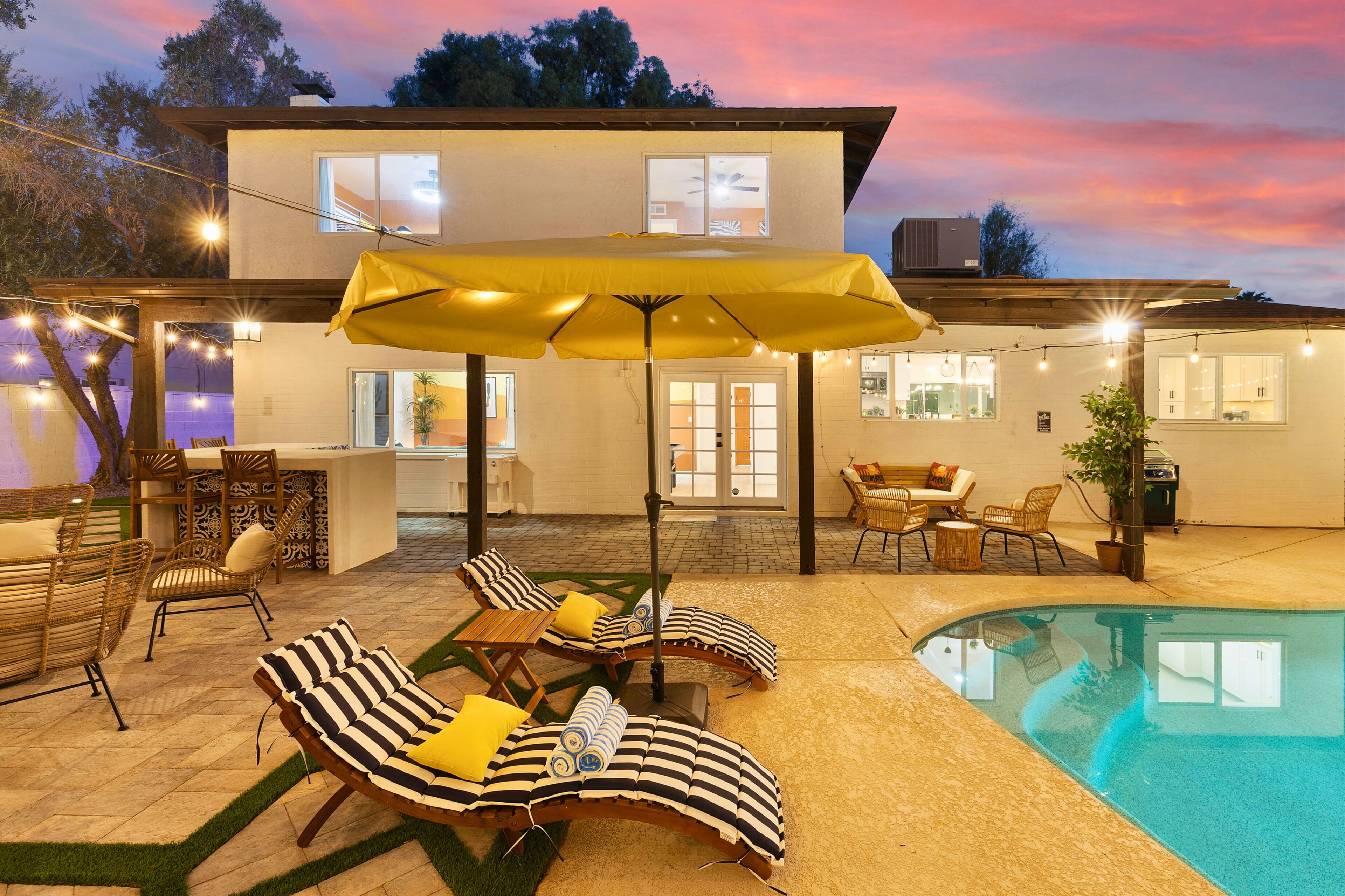 A poolside area with lounge chairs, a yellow umbrella, and a two-story building in the background.