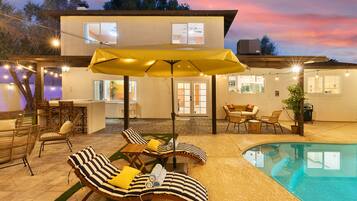 A poolside area with lounge chairs, a yellow umbrella, and a two-story building in the background.