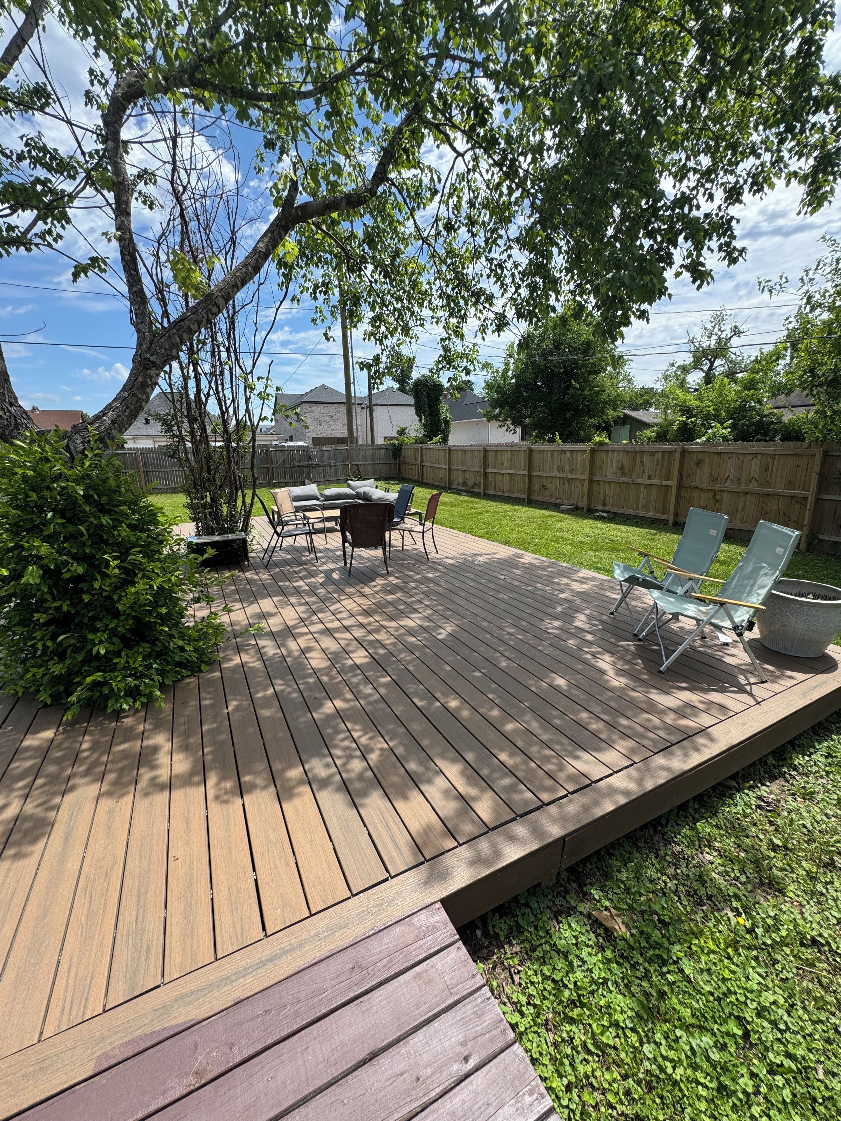 A wooden deck with a dining table and chairs, surrounded by a grassy yard and a wooden fence.