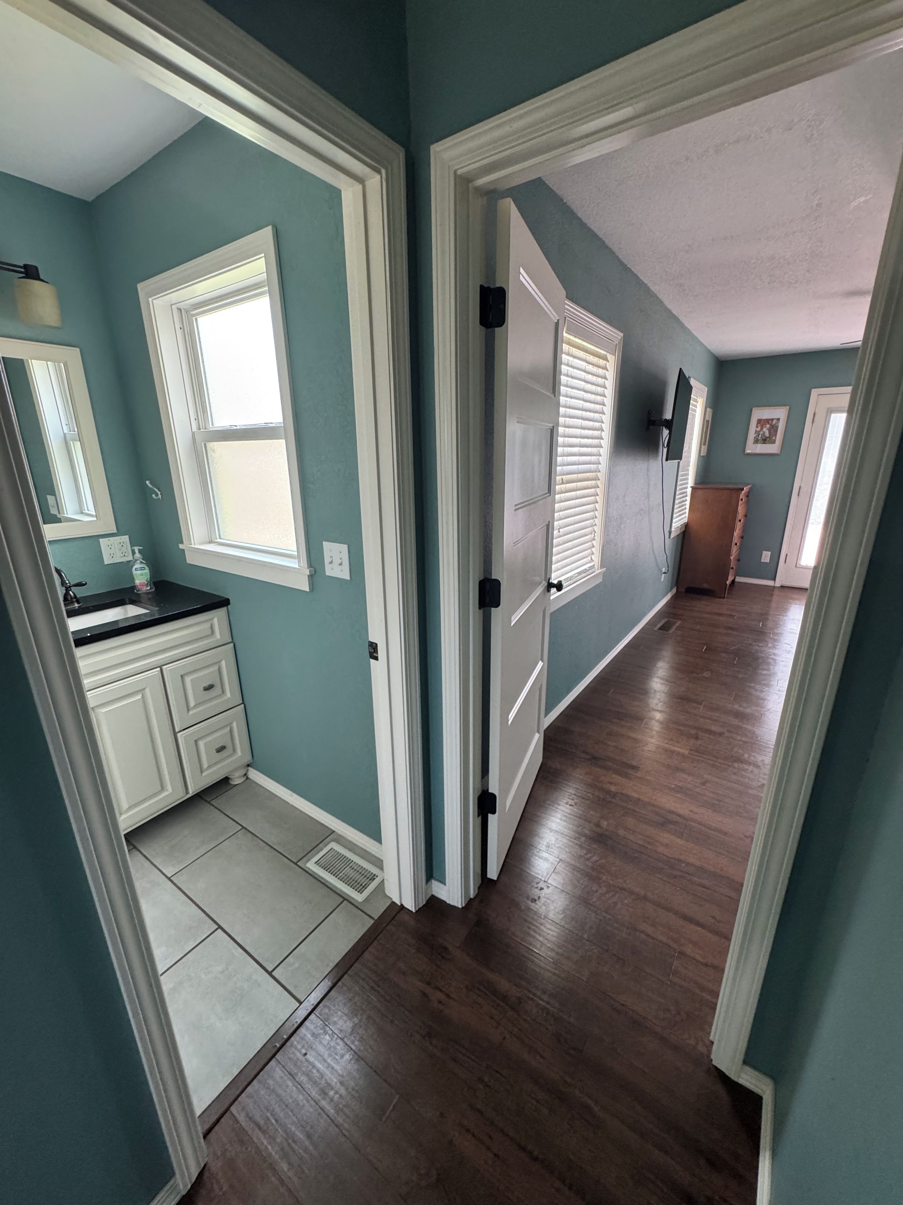 A hallway with a wooden floor, a white door, and a window with blinds.