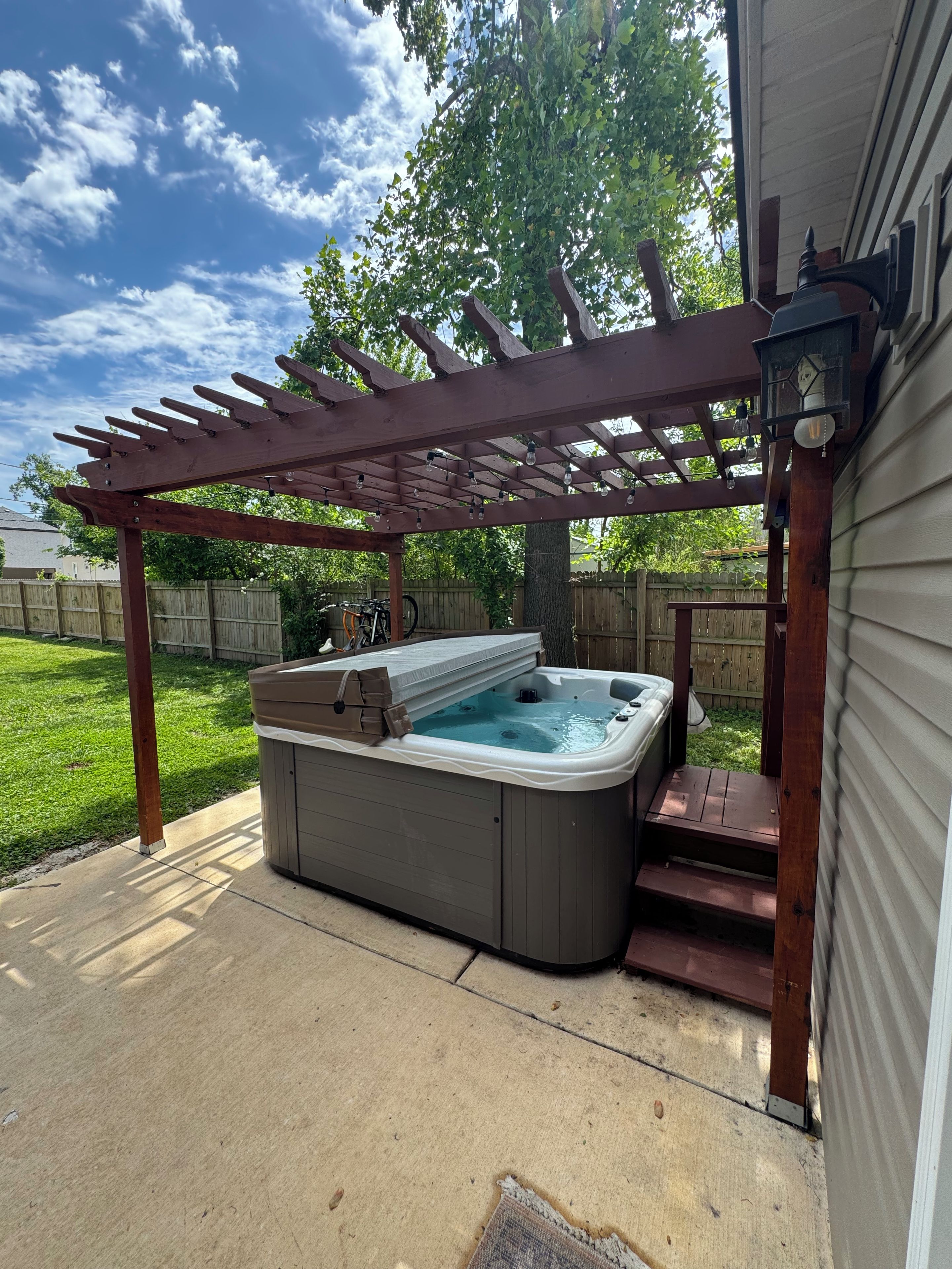 Un jacuzzi bajo una pérgola de madera, con cielo despejado al fondo.