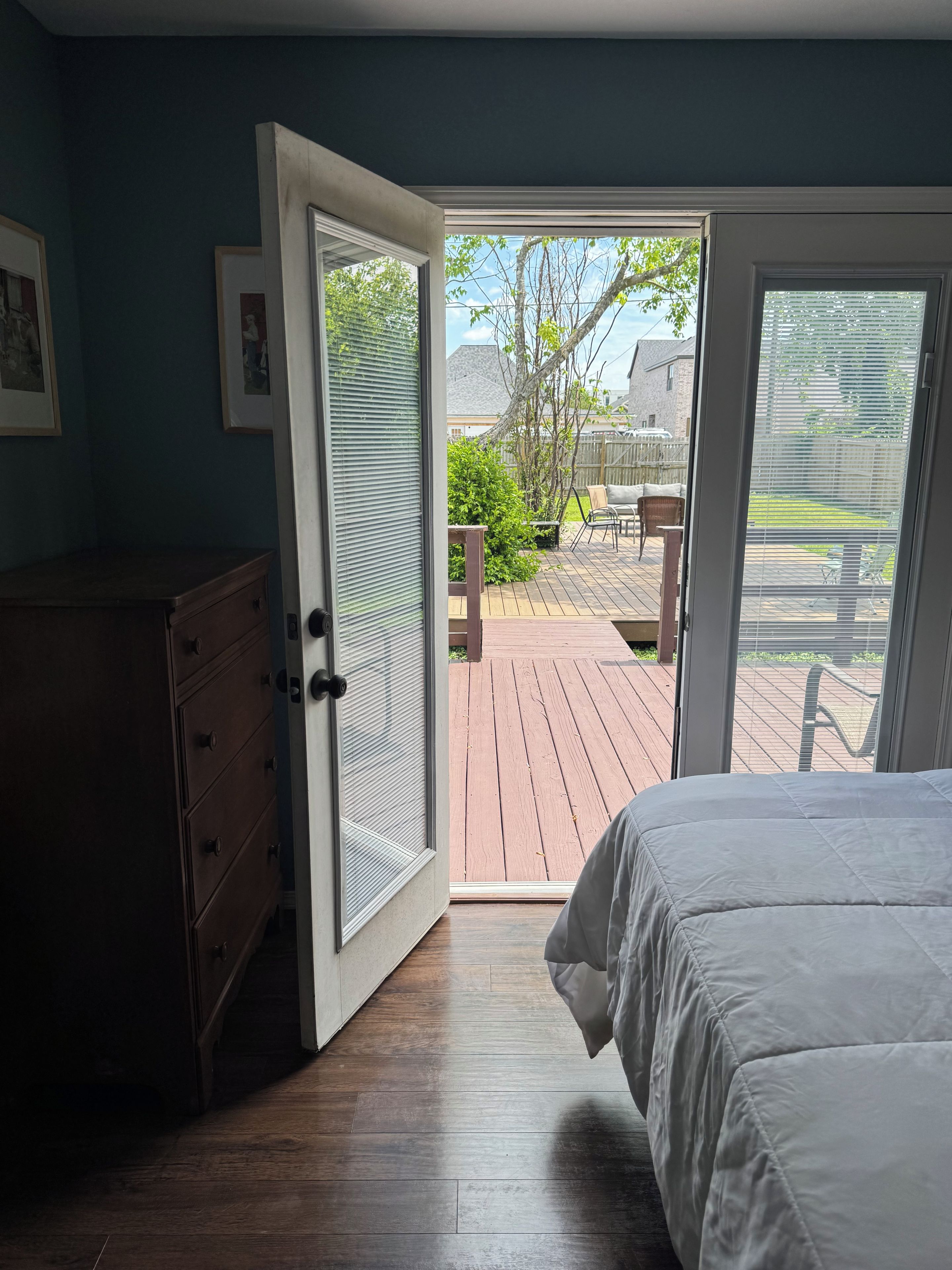 Quarto com cama, cômoda e porta de vidro corrediça que dá para um deck externo.