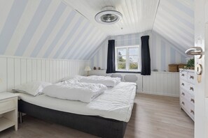 Ein Schlafzimmer mit Bett, Nachttisch, Kommode, einem Fenster mit Vorhängen und einem Deckenventilator.