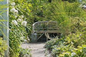 Un sendero conduce a un banco rodeado de abundante vegetación y plantas en flor.
