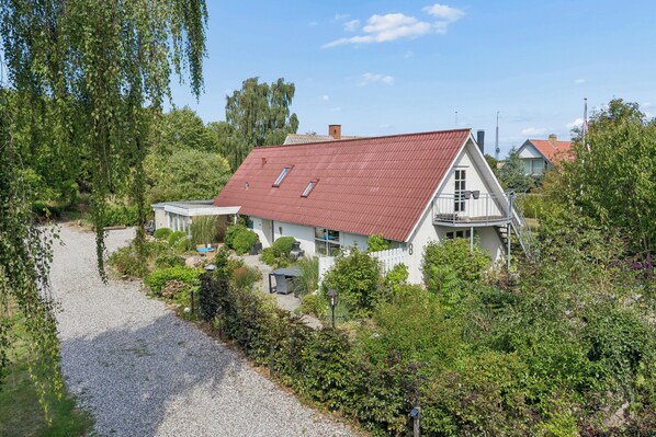 A house with a red roof, surrounded by greenery and a gravel path.