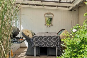 Ein überdachter Außenbereich mit Tisch, Stühlen, einem Dekospiegel und einem Grill.