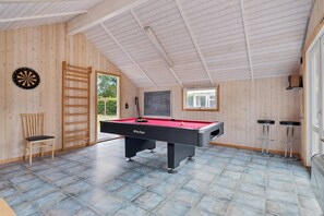 Huoneessa on biljardipöytä, tikanheitotaulu, tuoli ja ikkuna.