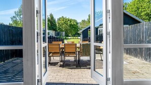An open patio with a table and chairs, a wooden fence, and a blue building in the background. - Holiday home by Limfjord, Storvorde (Storvorde)