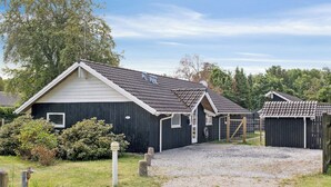 A row of small, dark-colored cabins with pitched roofs, surrounded by a gravel path and greenery. - Holiday home by Limfjord, Storvorde (Storvorde)