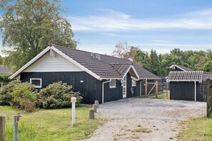Rivi pieniä, tummanvärisiä mökkejä, joissa on jyrkät katot. Mökit sijaitsevat sorapolun ja vehreyden ympäröimänä.