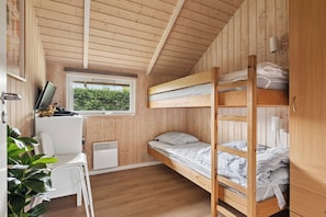 Une petite chambre comprenant un lit superposé, un bureau et une fenêtre donnant sur un espace verdoyant.