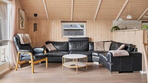 A cozy living room with a black leather sofa, a wooden chair, and a round coffee table. - Holiday home by Limfjord, Storvorde (Storvorde)