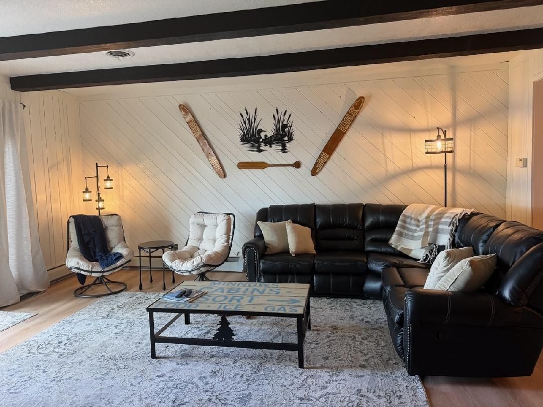 A living room with a black leather sofa, two white armchairs, a coffee table, and a patterned rug.