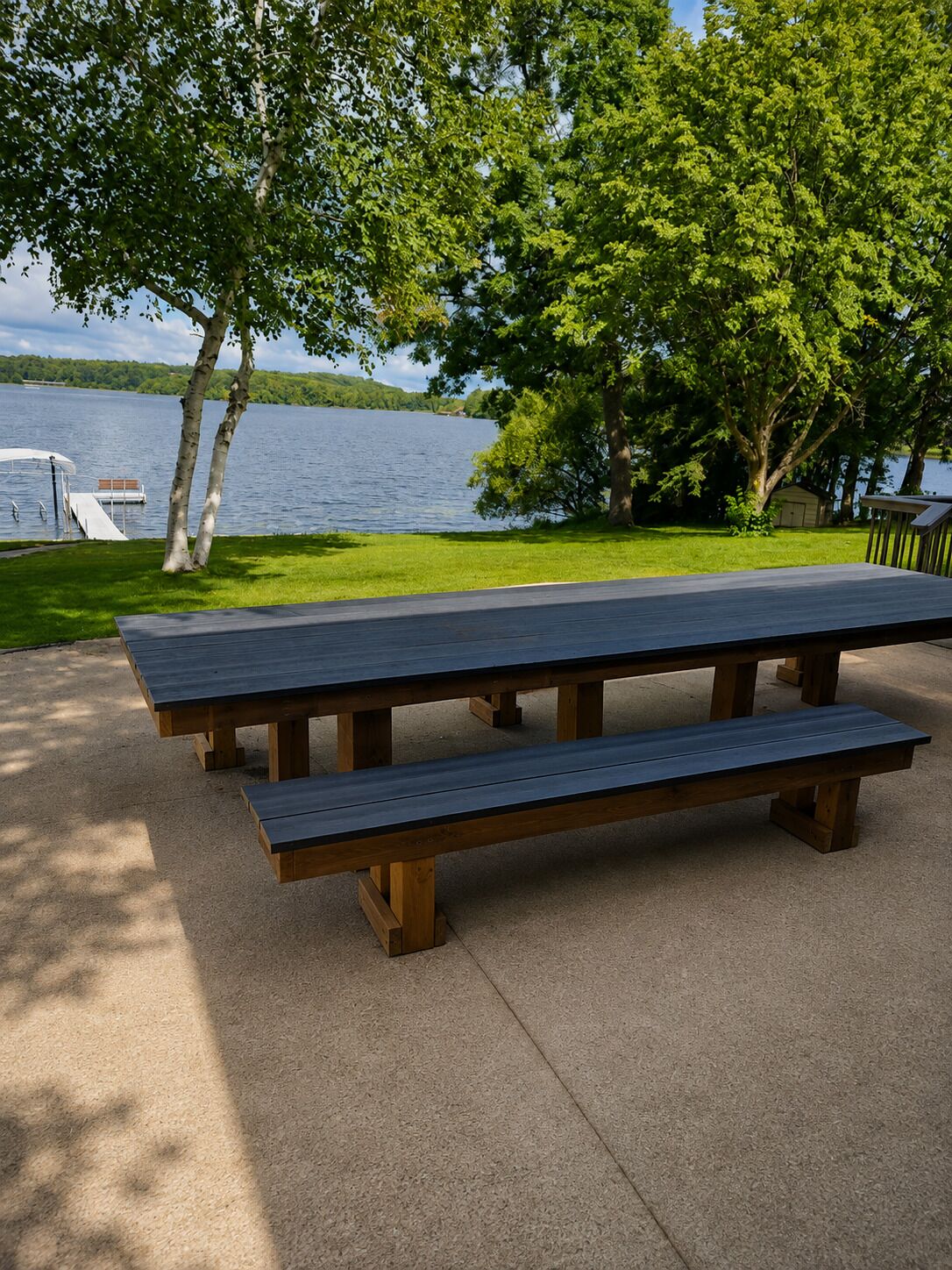 Mesa de piquenique com bancos, superfície de concreto e vista para um lago com um cais.