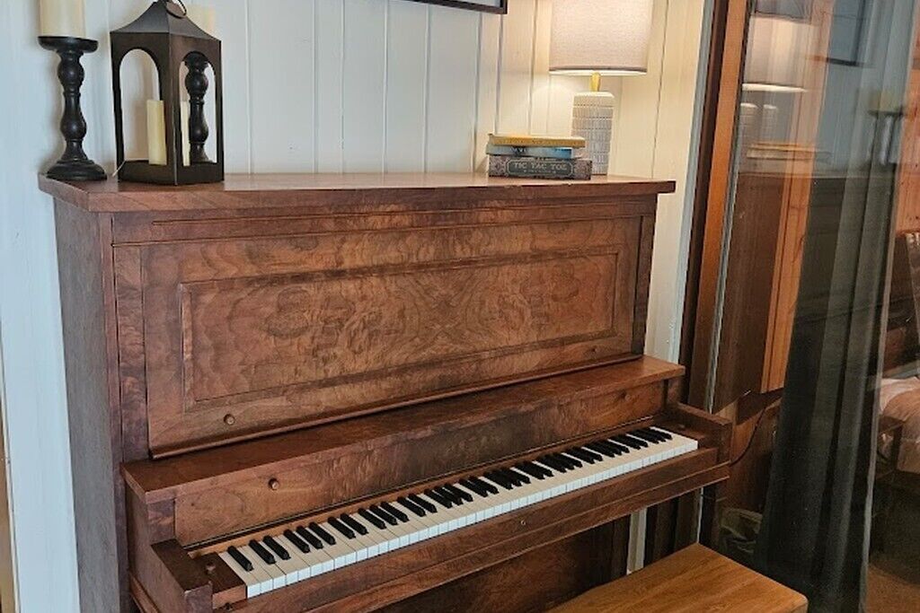 A wooden piano with a white keyboard, a candle holder, and a book on top.