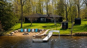 A lakeside property with a dock, outdoor seating, and a house.