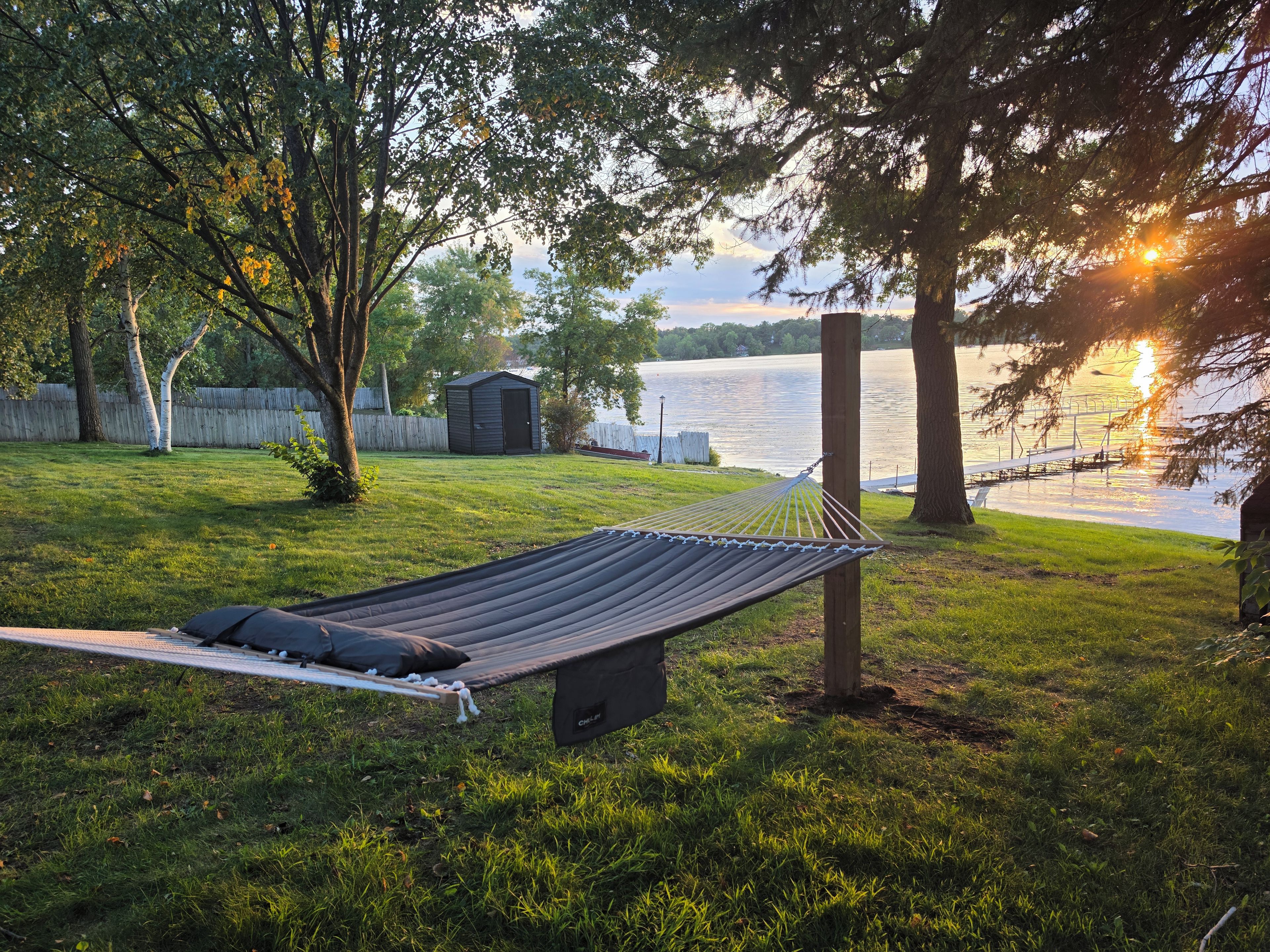 A hammock in a grassy yard with a lake view, a shed, and trees.