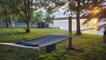 A hammock in a grassy yard with a lake view, a shed, and trees.