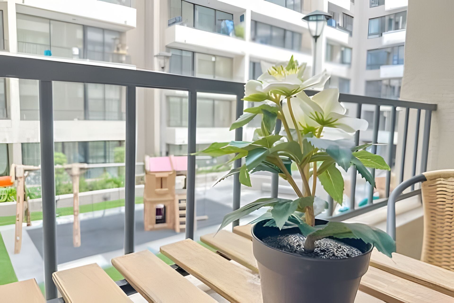 A balcony with a potted plant, wooden furniture, and a view of a modern building.