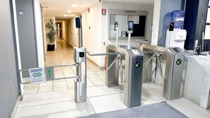 L’entrée d’un hôtel, avec un tourniquet, un panneau indiquant un accès prioritaire et un distributeur d’eau.