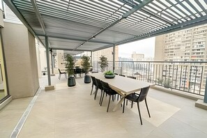 En inglasad balkong med ett matbord och stolar, krukväxter och utsikt över stadens byggnader.