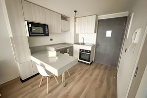 Une cuisine compacte équipée d’un four à micro-ondes, d’un évier et d’un four, un petit coin repas avec une table et des chaises, et une porte avec une poignée.