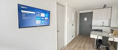 A modern kitchen with a built-in oven, a dining area with a table and chairs, and a wall-mounted TV displaying various apps.