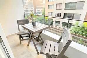 En balkong med ett bord och stolar, en krukväxt och utsikt över de omgivande byggnaderna.