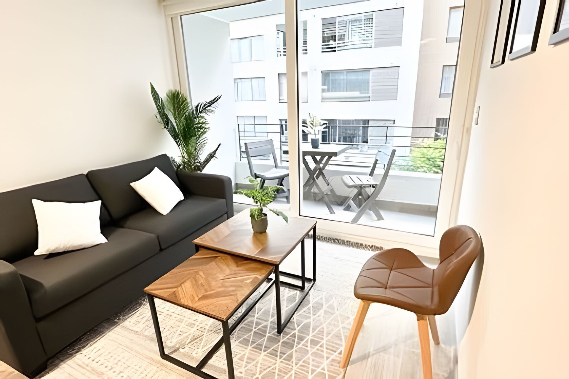 Una sala de estar moderna con un sofá, una mesa de centro, una silla y un balcón con mobiliario exterior.