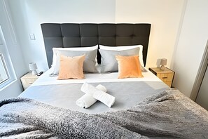 En snyggt bäddad säng med ett grått täcke, två kuddar och en hopvikt handduk.