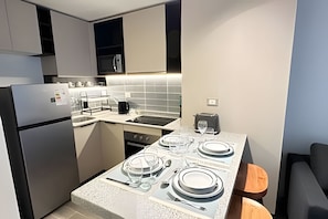 A compact kitchen with a refrigerator, microwave, stove, and a dining area set for four. - Downtown apartment steps from Santander Arena (Santiago)