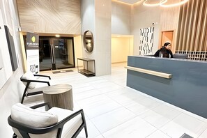 Ett modernt receptionsområde med en receptionsdisk, stolar och en entré med glasdörr.