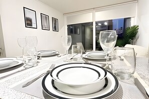 Ett matbord dukat med tallrikar, glas och bestick, med utsikt över staden genom en glasdörr.