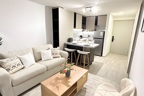 A modern living room with a sofa, coffee table, and a small kitchen area with a bar and stools. - Central apartment | Near Santander Arena | Wi-Fi (Santiago)