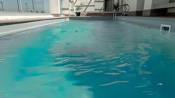 Ein Swimmingpool mit klarem Wasser, eine Poolleiter und ein Gebäude im modernen Architekturstil im Hintergrund.