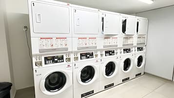 Une laverie équipée de plusieurs machines à laver et de plusieurs séchoirs, chacun étant doté d’un panneau de commande et d’un numéro d’identification.
