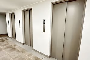 A hallway with four elevators, each with a metallic control panel. - Central apartment | Near Santander Arena | Wi-Fi (Santiago)