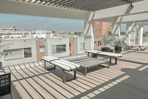 Une terrasse sur le toit avec une plateforme en bois, deux chaises longues, une table en métal et des plantes en pot.