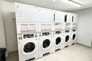 A laundry facility with multiple washing machines and dryers, each with a control panel and numbered for identification. - Central boutique apartment steps from Movistar|WIFI (Santiago)